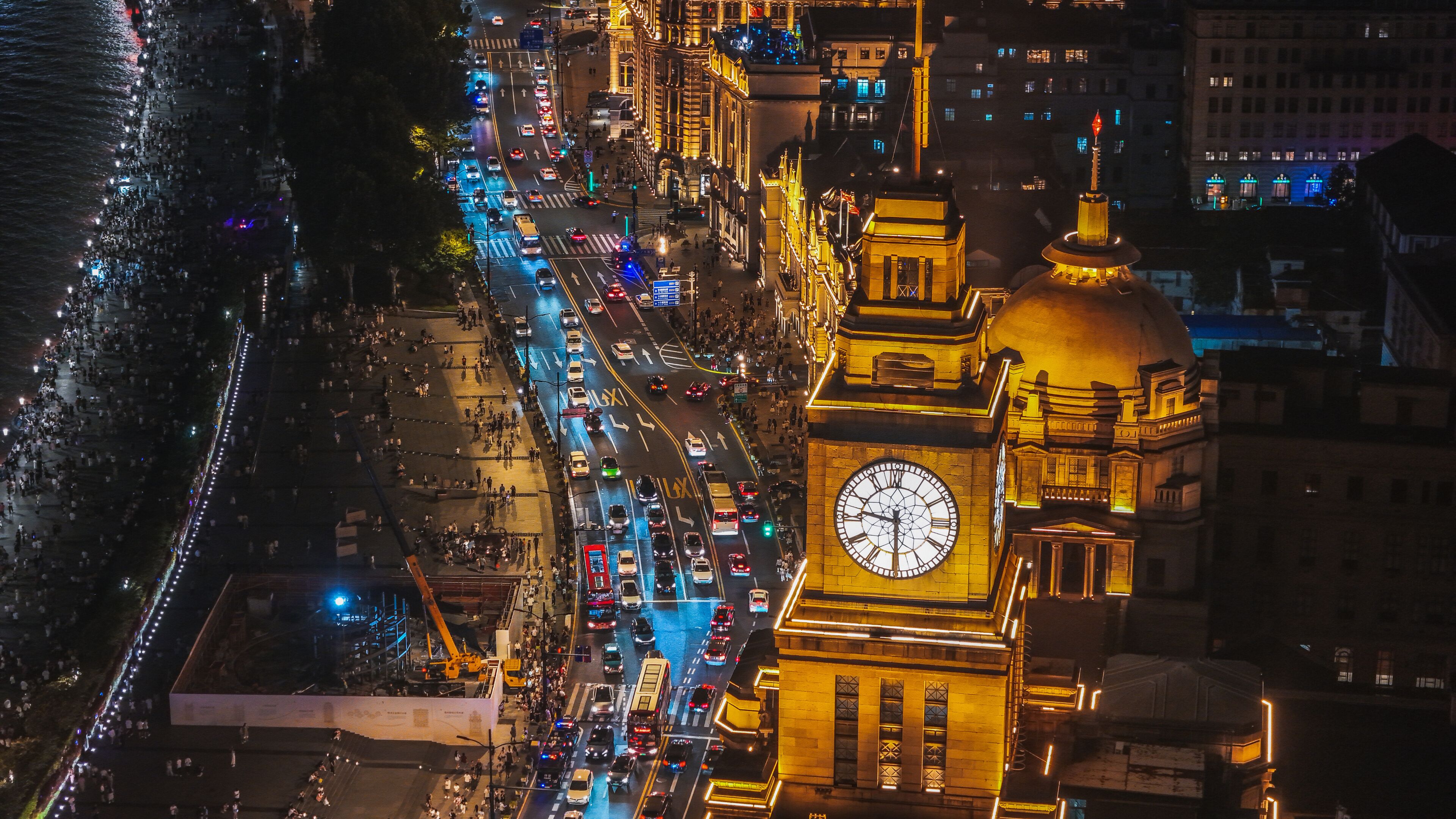 Una concurrida calle urbana de noche, con una destacada torre de reloj y edificios iluminados.