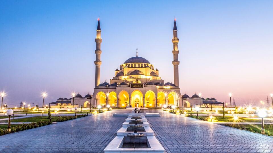 A mosque with two minarets, a large central dome, and a courtyard with a water feature.