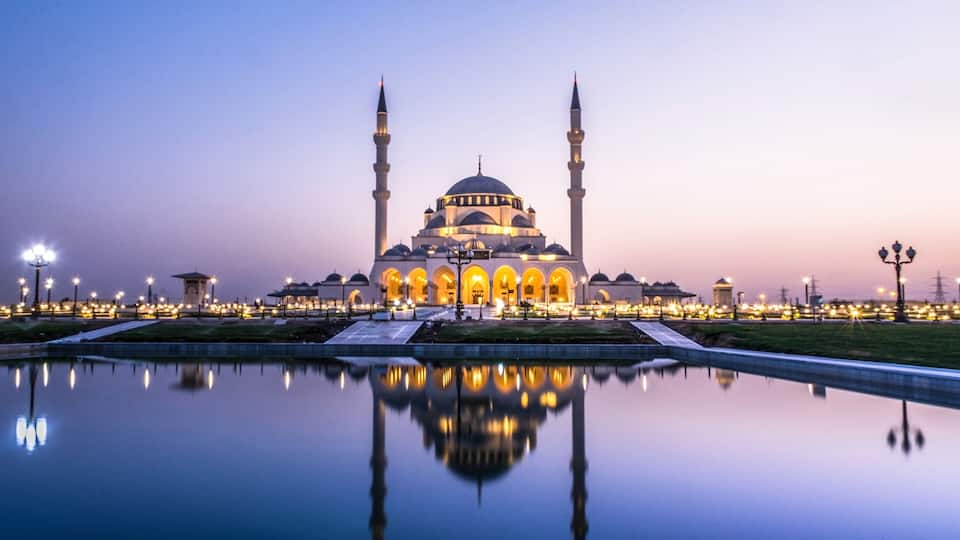 A mosque with two minarets, a large central dome, and a reflection in the water.