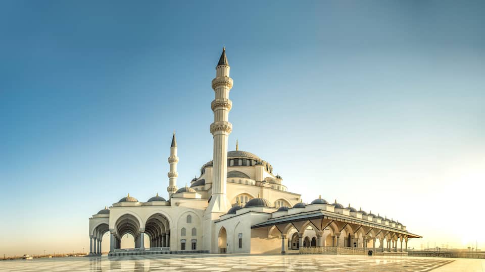 A large mosque with multiple domes and minarets, a spacious courtyard, and a clear blue sky.