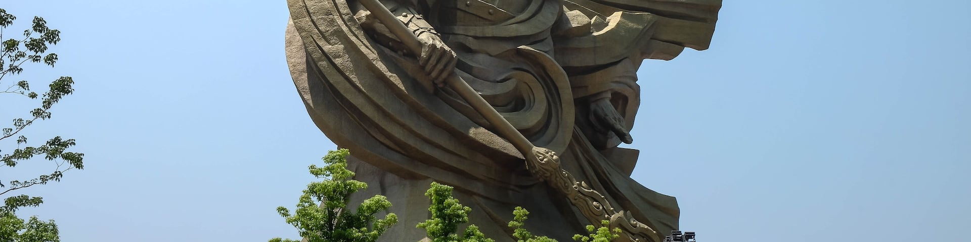 A large, ornate statue of a warrior with a spear, set against a clear blue sky.