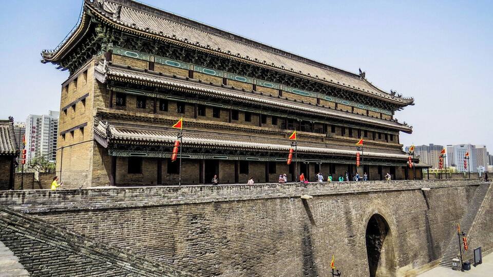 A traditional multi-tiered building with a tiled roof and a brick wall with a gate.