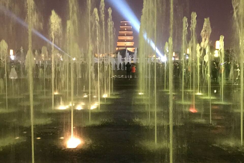A night scene with a water fountain display and a pagoda in the background.