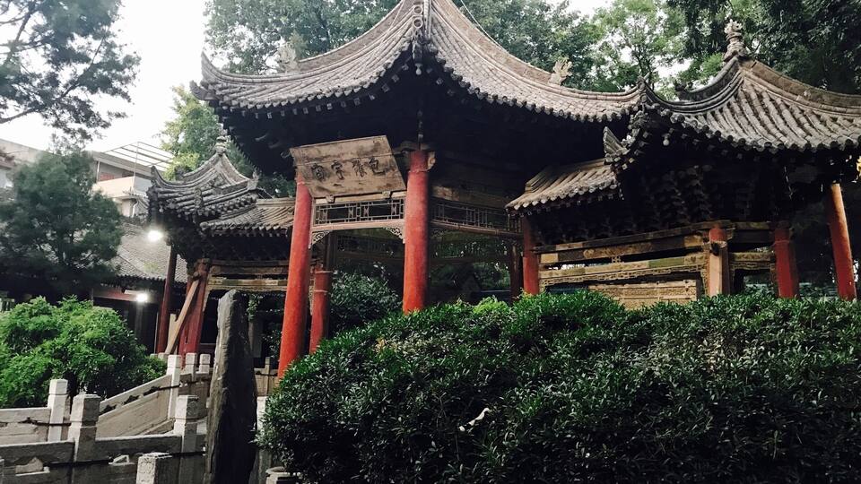 A traditional Chinese pavilion with ornate roofs and red pillars, surrounded by lush greenery.