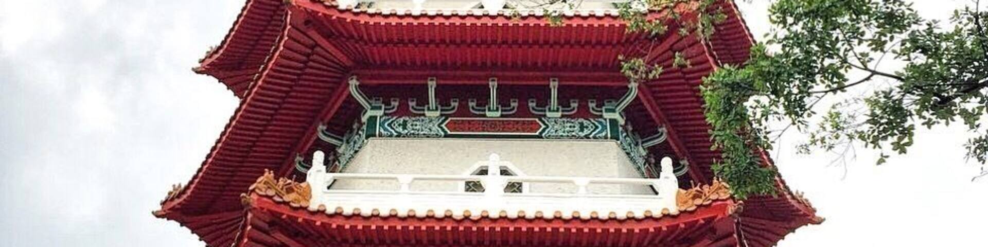Un pagodas de varios niveles con tejados rojos y blancos, rodeado de exuberante vegetación.