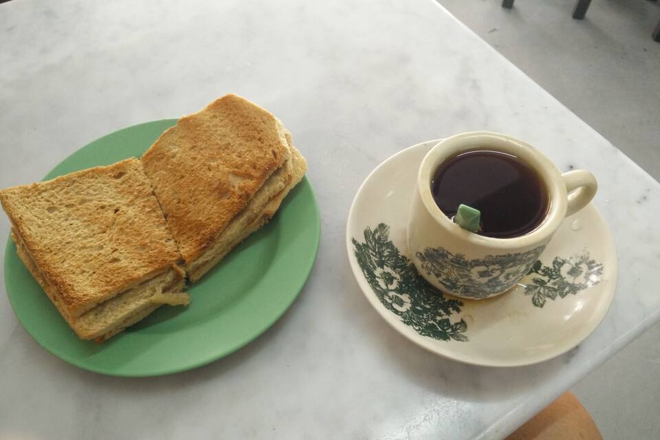Un plato verde con pan tostado y una taza de café negro sobre una mesa blanca.