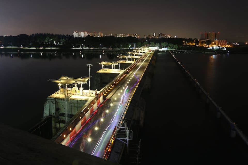 Vista nocturna d'un pont amb marques de carretera il·luminades i un perfil urbà al fons.