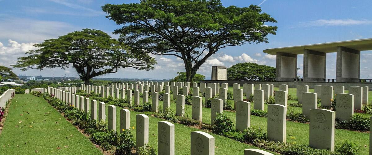 A cemetery with rows of headstones, a large tree, and a building in the background.