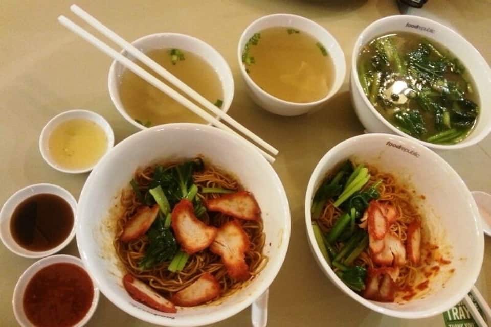 A table with various bowls of Asian noodle dishes, including noodles with vegetables and meat, and several small bowls of sauces and broth.
