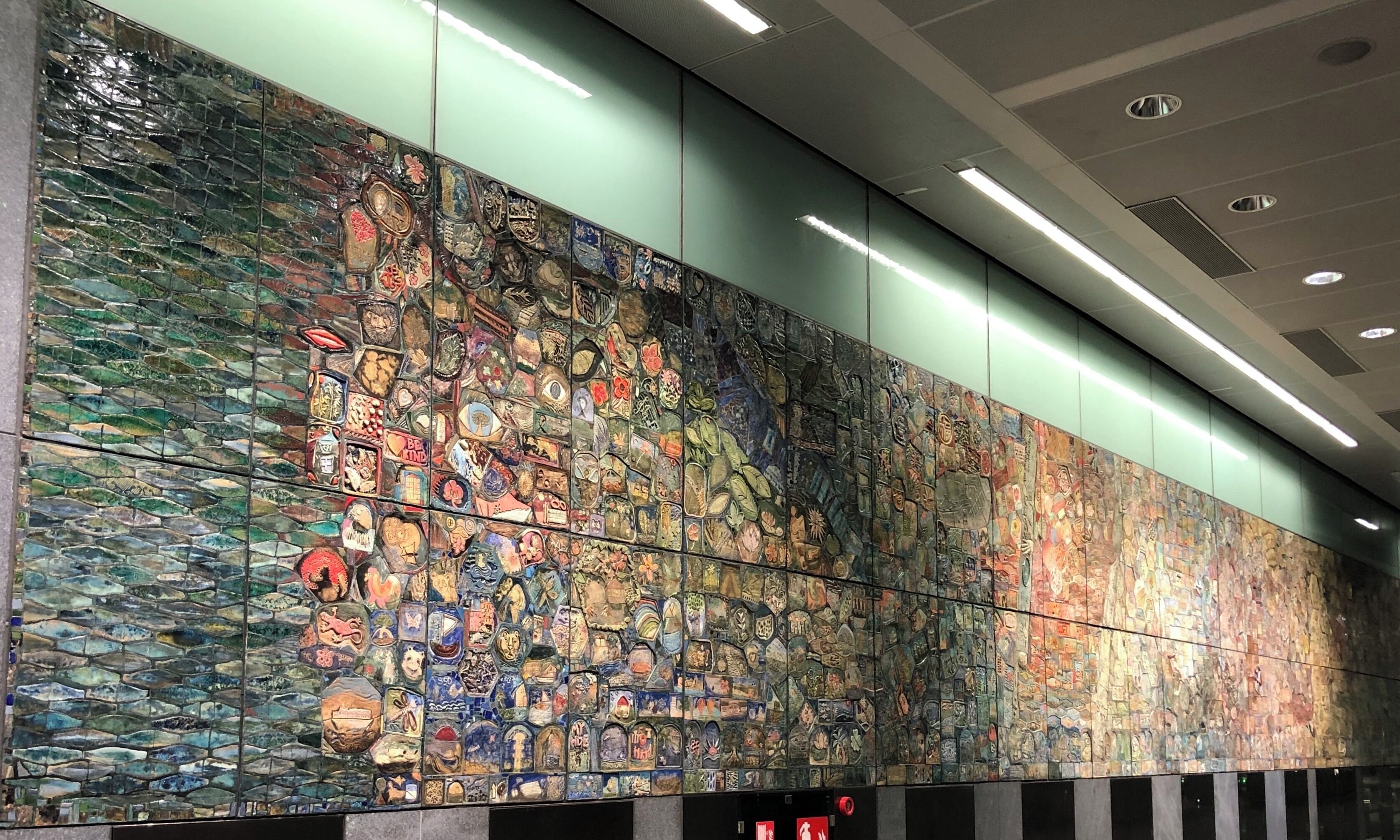 The mural is made of a series of oven-fired clay tiles, a composite artwork by nearly 1,500 participants. People from all walks of life were invited to make clay representations of what they see as the Singapore story over the course of six months. Located at the Marina South Pier MRT Station. 