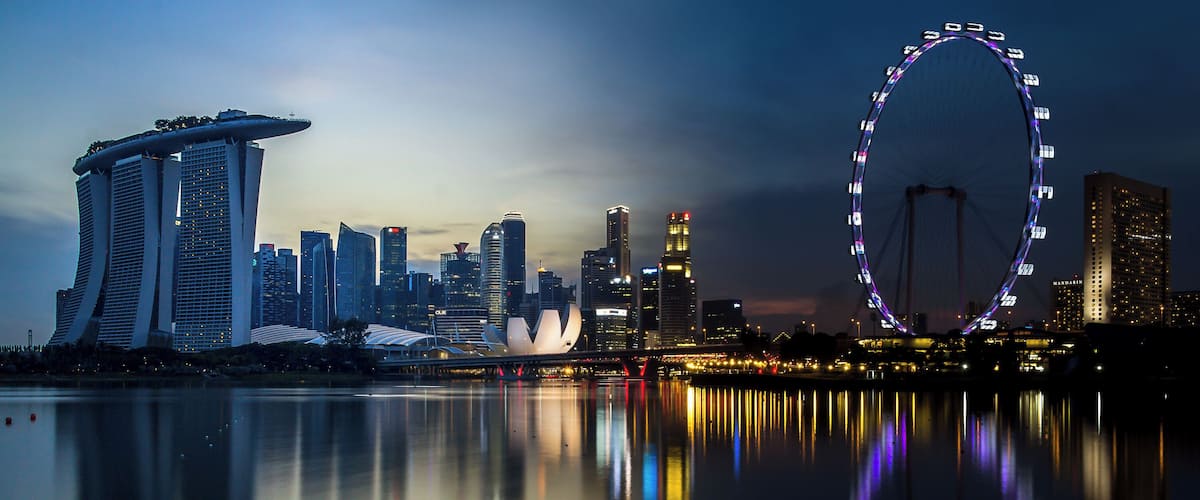 A city skyline with a prominent Ferris wheel and the Marina Bay Sands hotel reflected in the water.