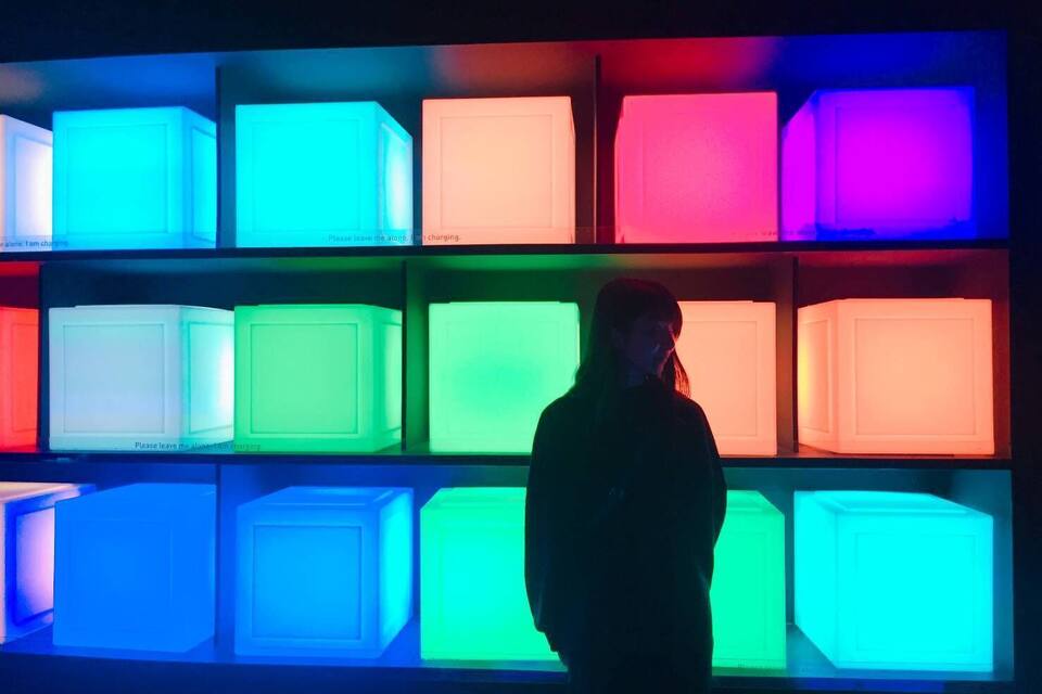 Una persona de pie frente a una pared de cubos iluminados en varios colores.