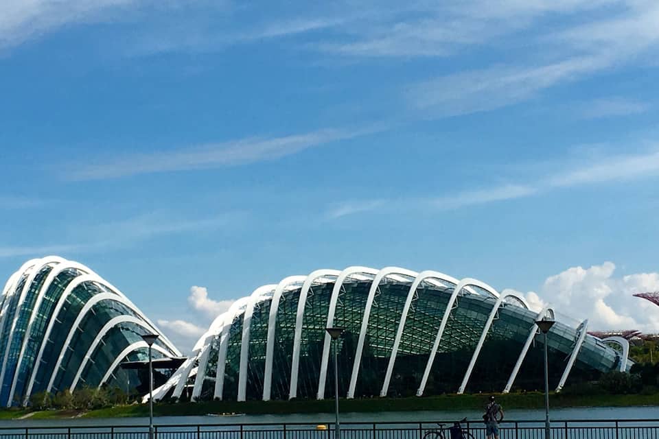 A modern architectural structure with a curved design, a body of water in the foreground, and a clear blue sky.