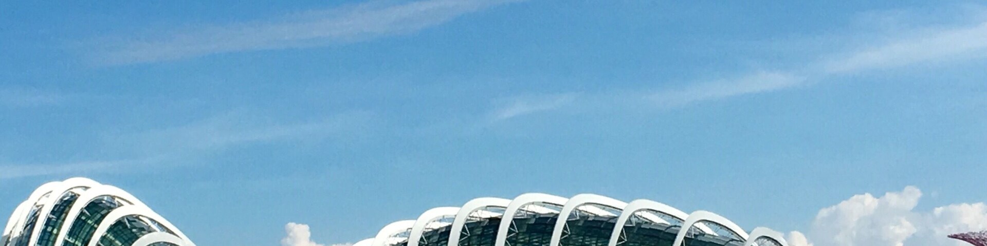 Una estructura arquitectónica moderna con un diseño curvo, un cuerpo de agua al frente y un cielo azul despejado.