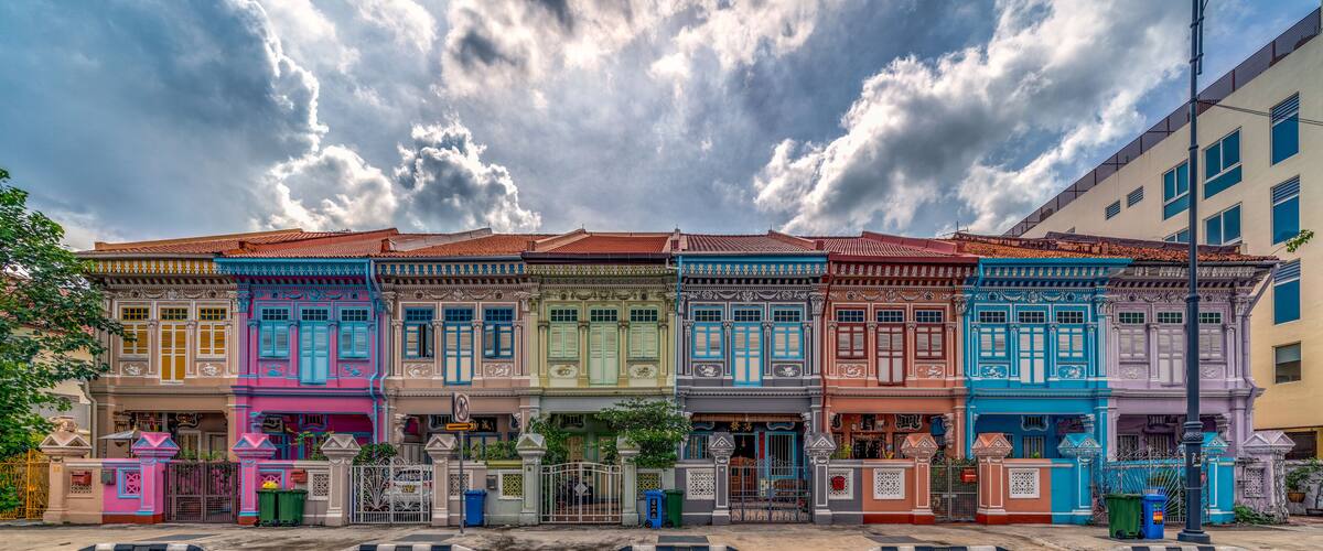 A row of colorful traditional buildings with ornate facades and a cloudy sky above.