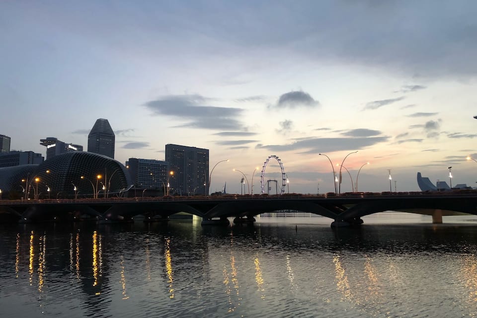 A bridge over water with city buildings and a Ferris wheel in the background.