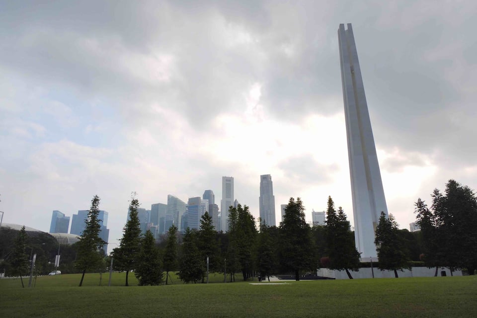 Ein Park mit einem hohen Denkmal und einer Stadtlandschaft im Hintergrund.