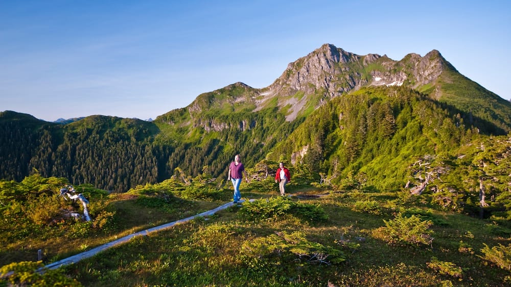 Un paysage montagneux avec un ciel dégagé, un sentier de randonnée et deux randonneurs.