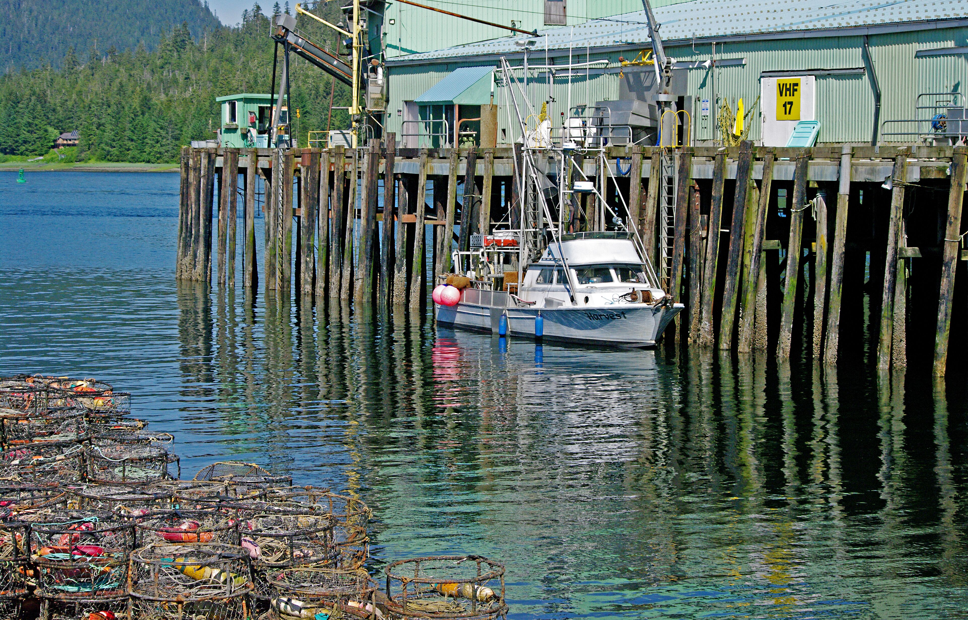 View of dock, fishing boat and stack of fishing traps.