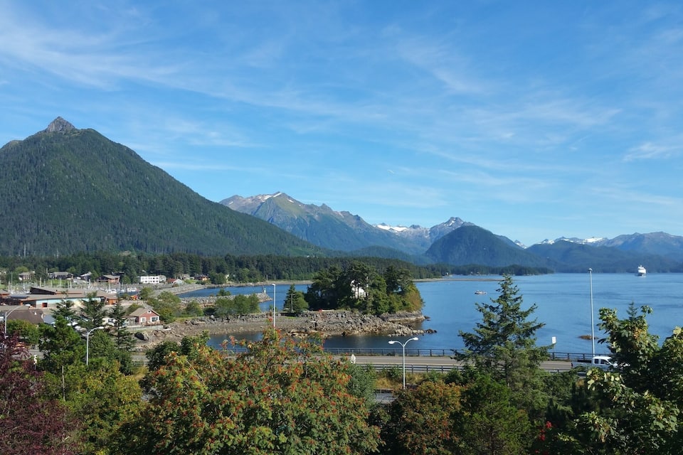 A coastal town with mountains in the background, a lake, and a ferry in the distance.