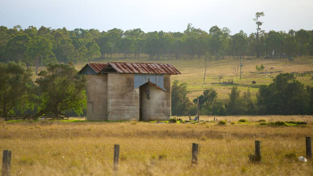 A rustic barn in a grassy field with a hilly landscape in the background.
