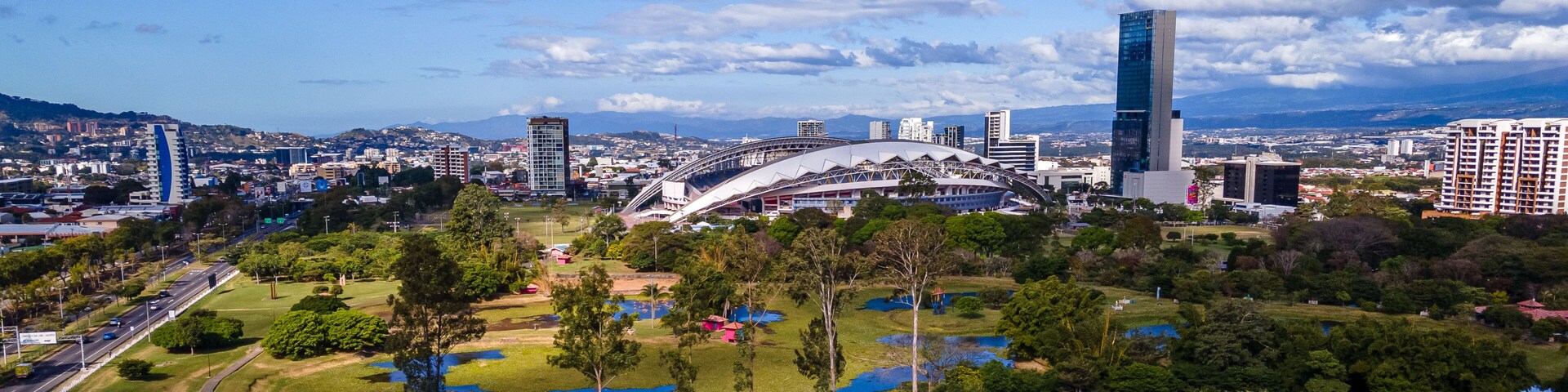 Paisagem urbana com um estádio em destaque, arranha-céus modernos e parques verdejantes.