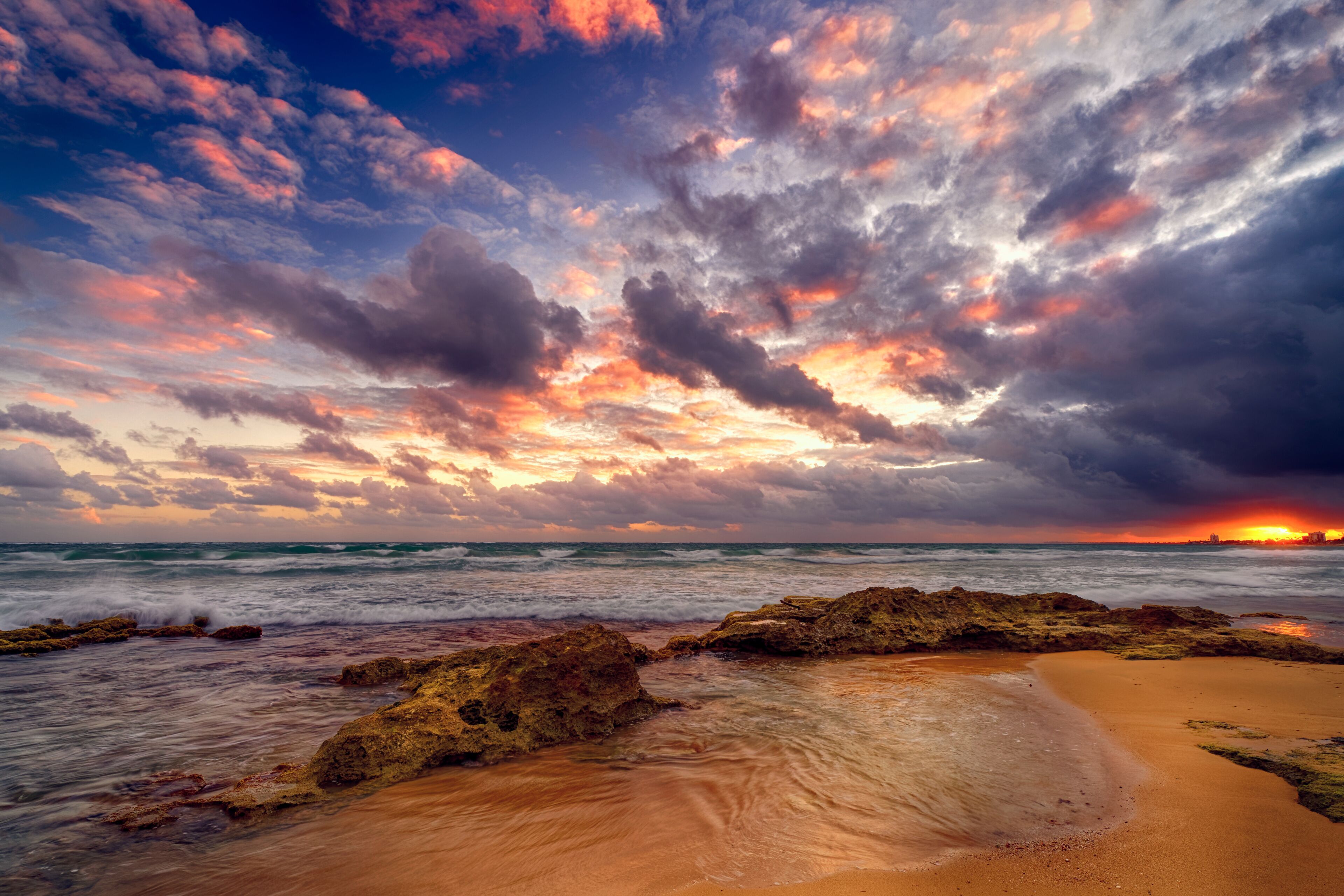 Una playa con rocas, olas y un atardecer.