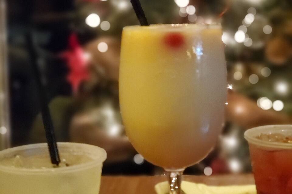 Um copo de bebida amarela com canudo e um copo de plástico com a palavra 'BORON' escrita, em frente a uma árvore de Natal desfocada.