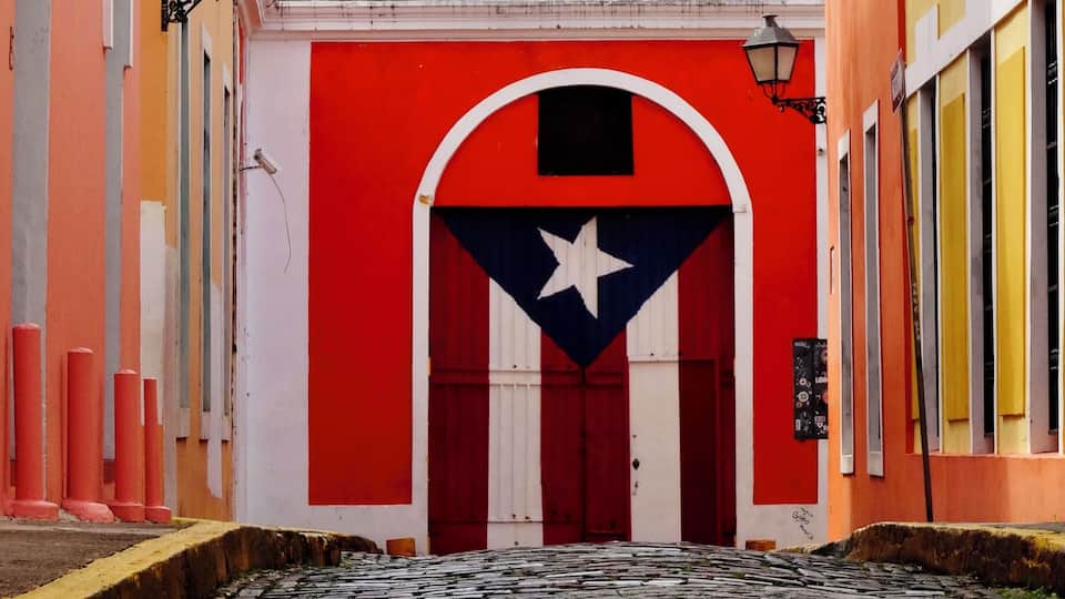 A cobblestone street with colorful buildings, a red door with a white star, and a white wall with a black star.