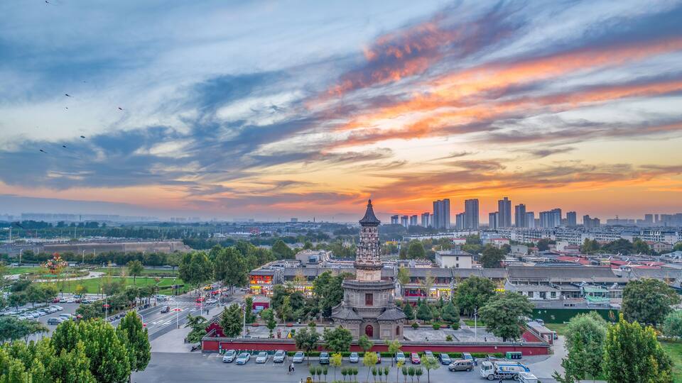 Un paisaje urbano con una torre tradicional, rascacielos modernos y un cielo al atardecer.