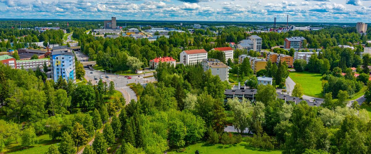 A cityscape with a mix of residential and commercial buildings, surrounded by lush green parks and trees.