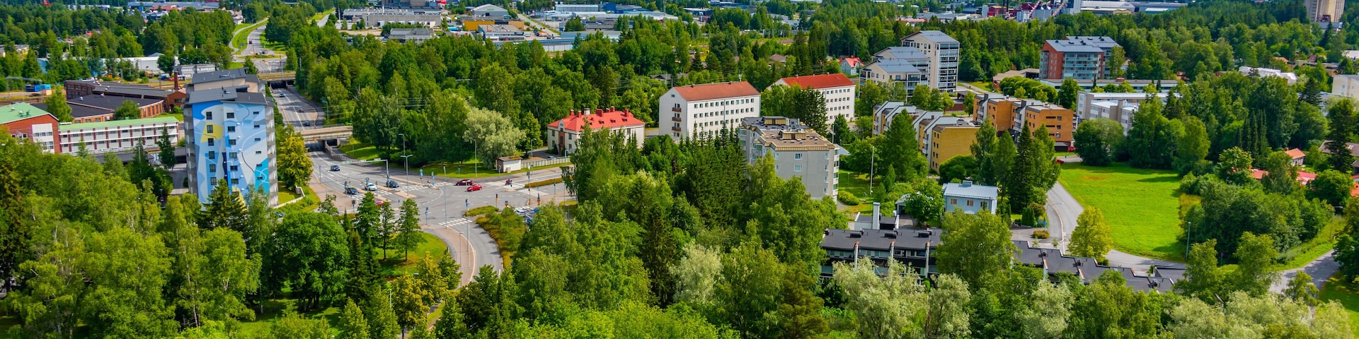 A cityscape with a mix of residential and commercial buildings, surrounded by lush green parks and trees.