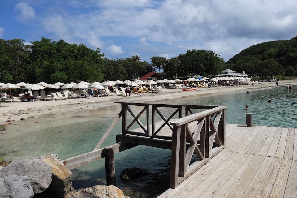 A beach with wooden walkways, umbrellas, and people swimming.