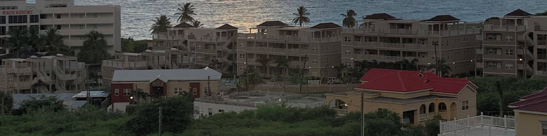 A coastal cityscape with buildings, palm trees, and a sunset over the ocean.