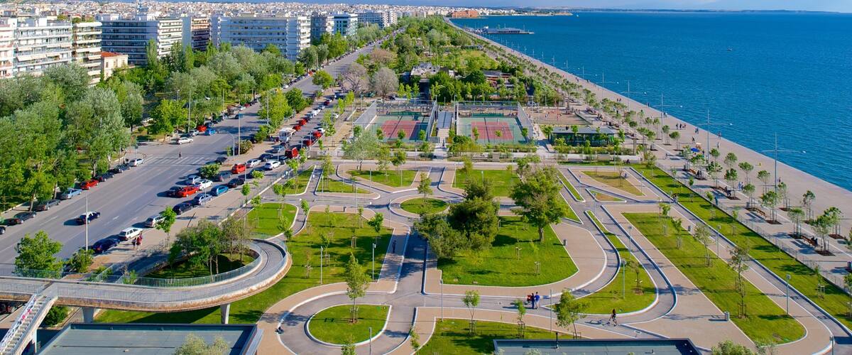 An aerial view of a coastal urban area with a curved road system, green spaces, and a waterfront.