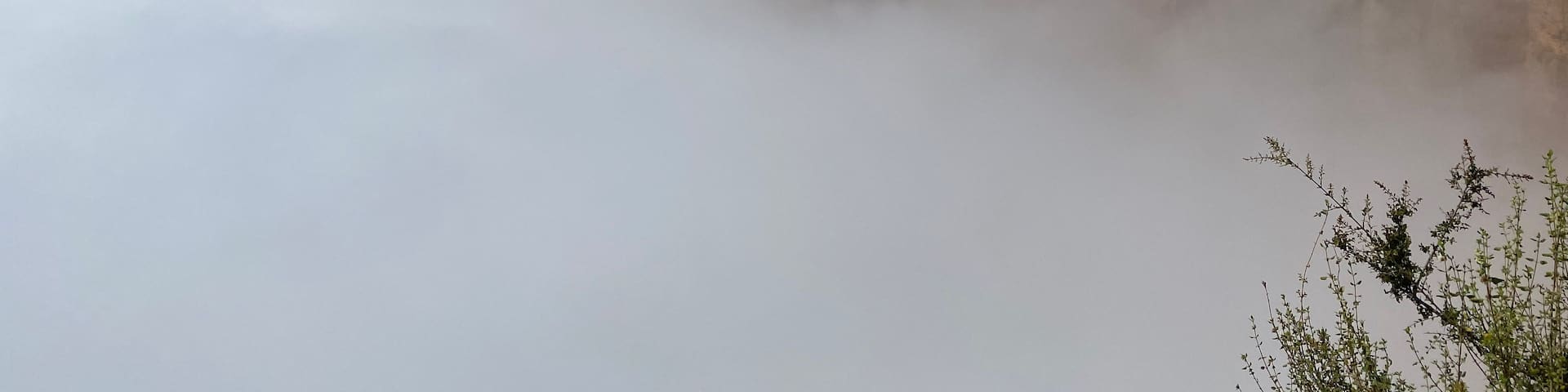 A rocky cliff with a building on top, surrounded by mist and a distant mountain range.