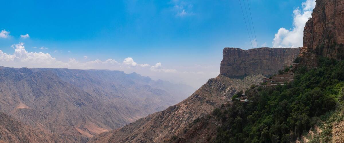 A mountainous landscape with a steep cliff on the right and a valley in the center.