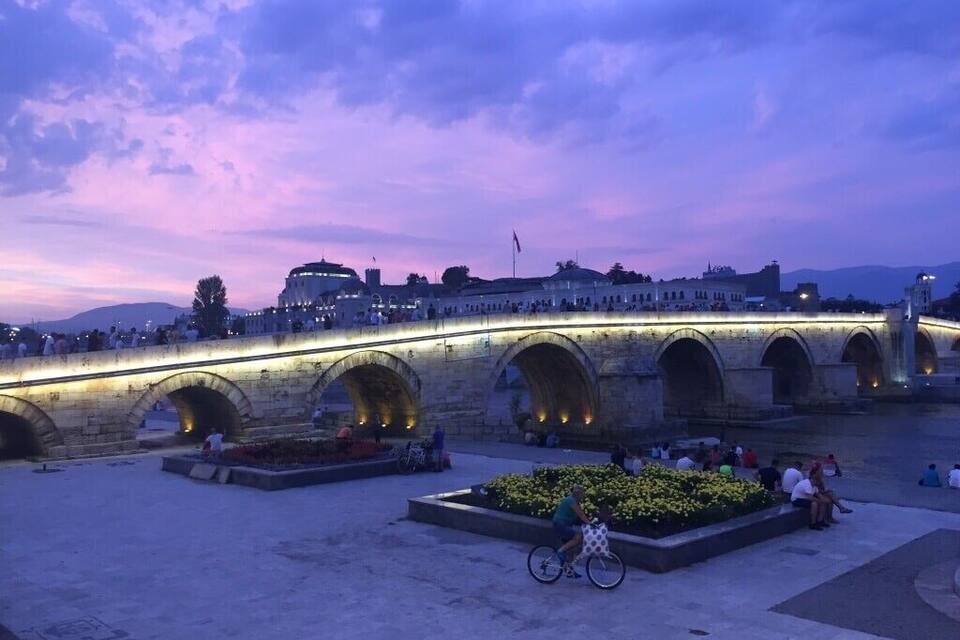 A stone bridge with arches, a flower bed, and a cyclist.