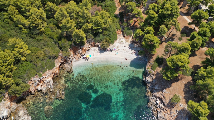 Vista aérea de una playa con aguas turquesas cristalinas, rodeada de árboles verdes y terreno rocoso.