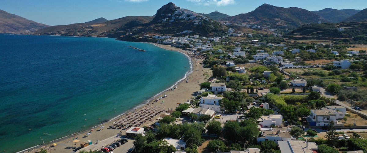 A coastal town with a beach, white houses, and mountains in the background.
