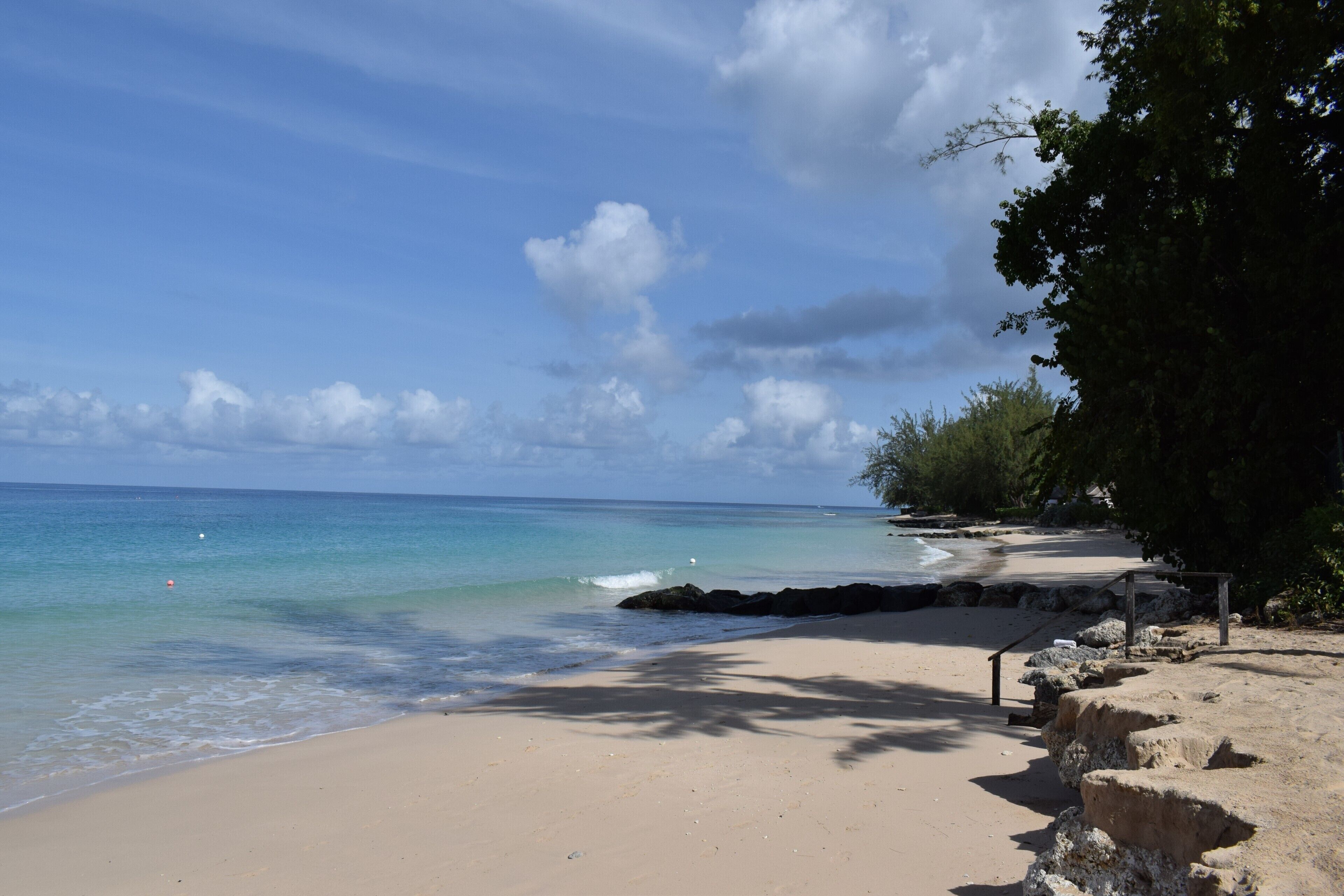 A beach with clear turquoise water, a sandy shore, and a rocky outcrop with a wooden structure.