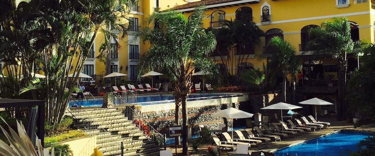 A resort with a swimming pool, palm trees, and a yellow building.