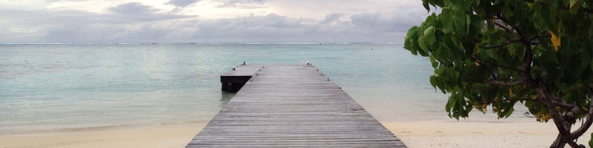 A wooden pier extending into a calm sea with a sandy beach and a cloudy sky.