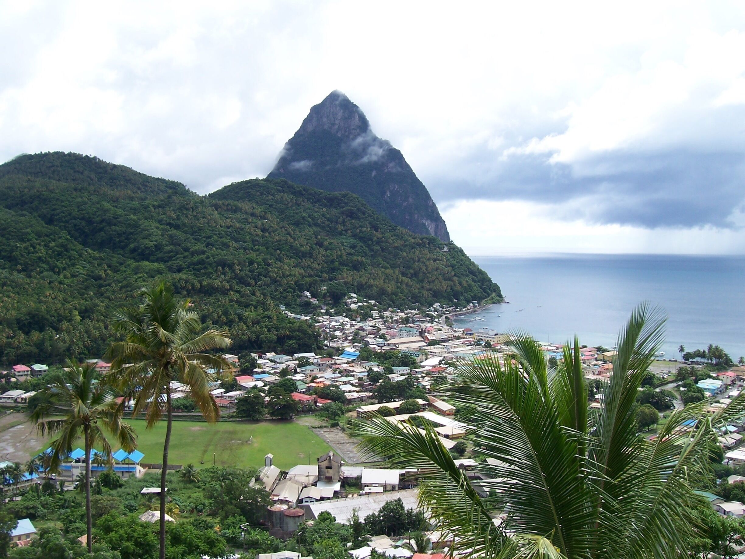 A coastal town with a prominent mountain peak, lush greenery, and a beach.