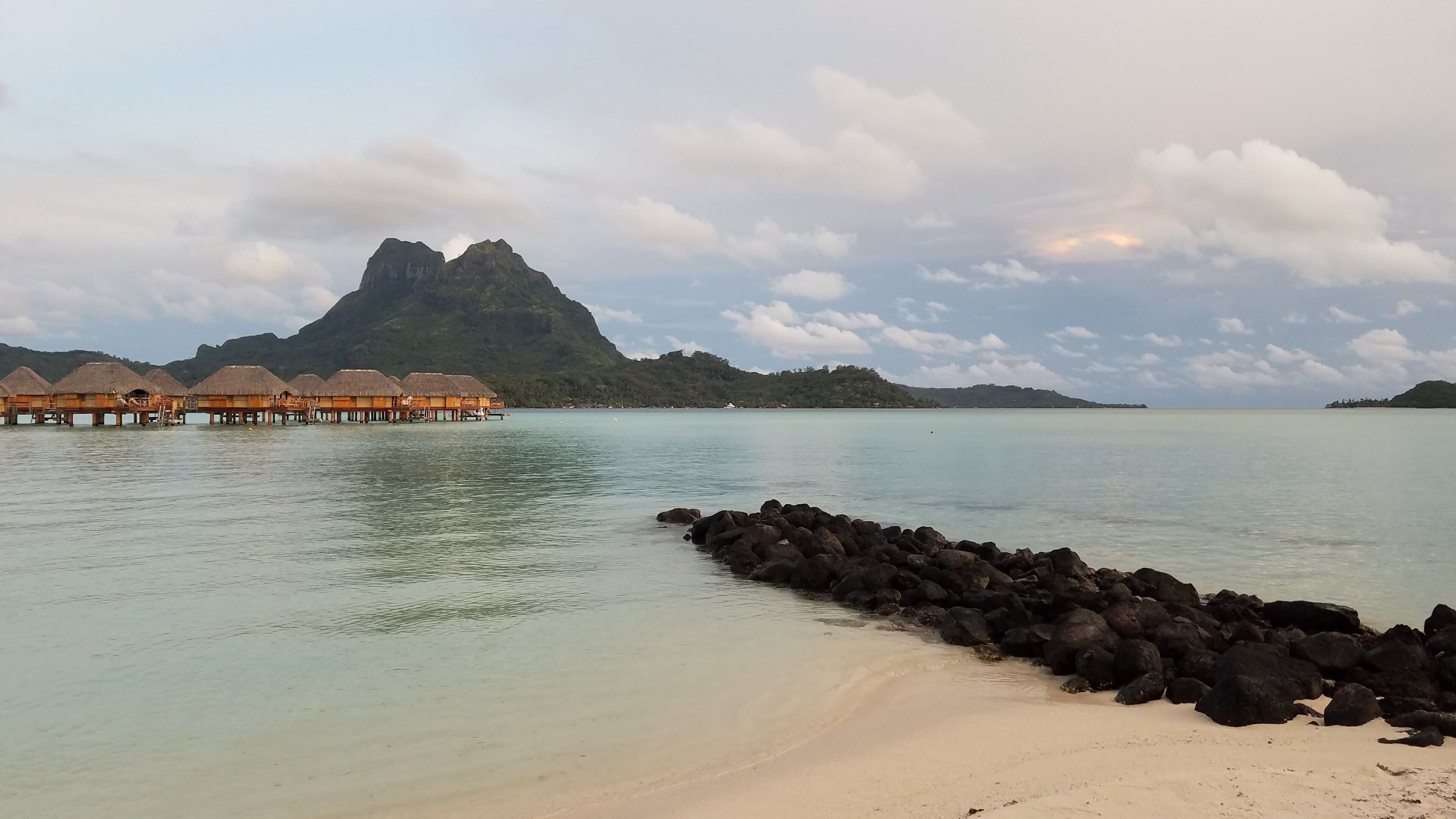 A beach with overwater bungalows and a rocky breakwater.
