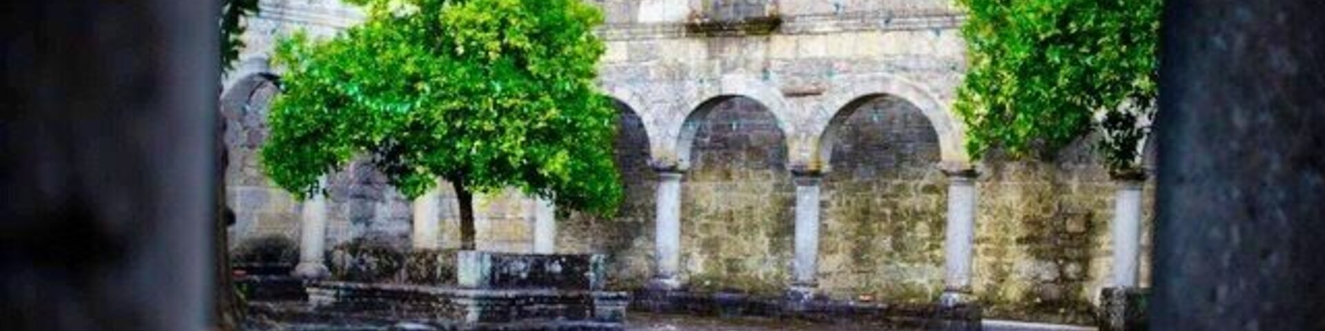 Un patio con bancos de piedra, árboles y un muro de piedra con arcos.
