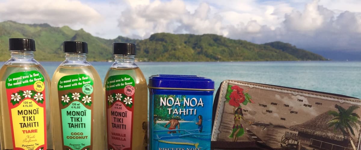 Three bottles of Monoi Tahiti, a tin of Noa Noa Tahiti biscuits, and a postcard with a tropical scene.