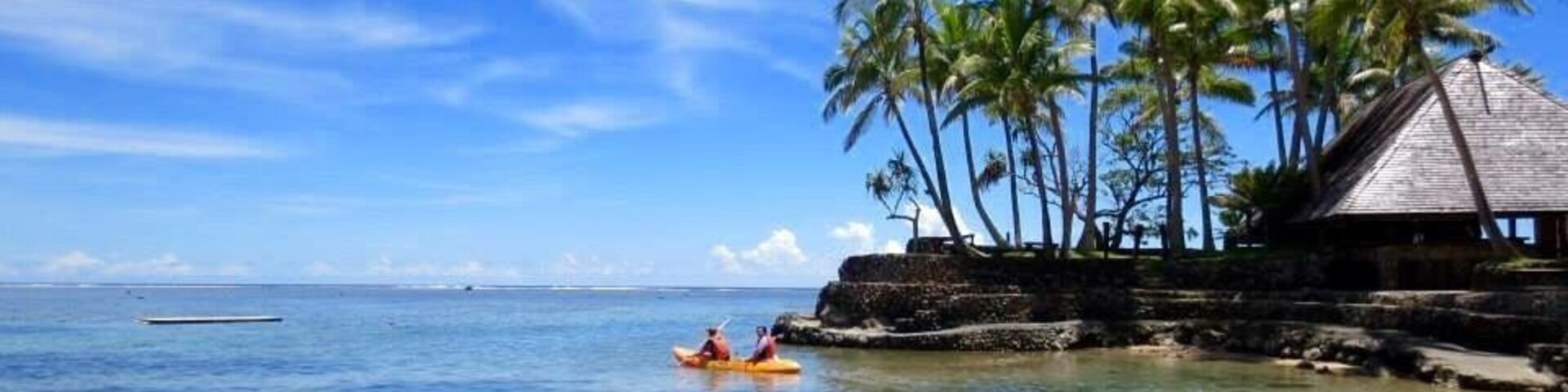Una playa con agua azul cristalina, una cabaña de techo de paja y palmeras.