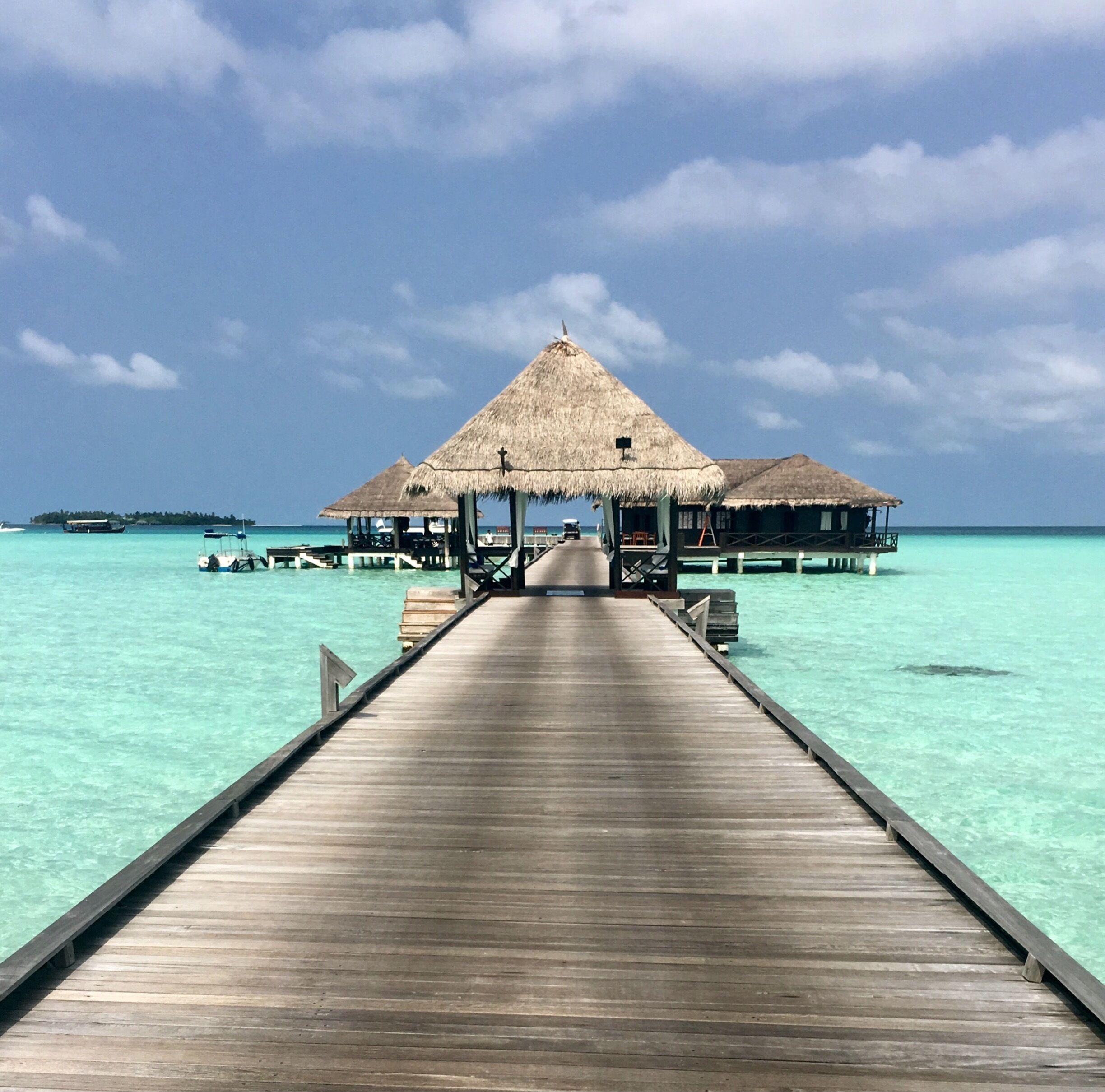 A wooden pier leading to overwater bungalows with thatched roofs.