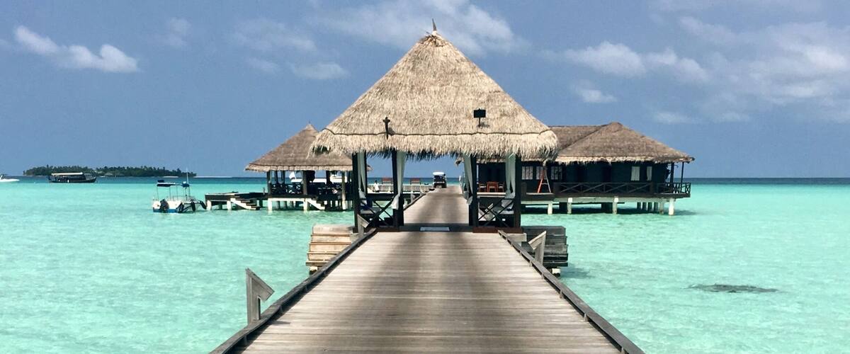 A wooden pier leading to overwater bungalows with thatched roofs.